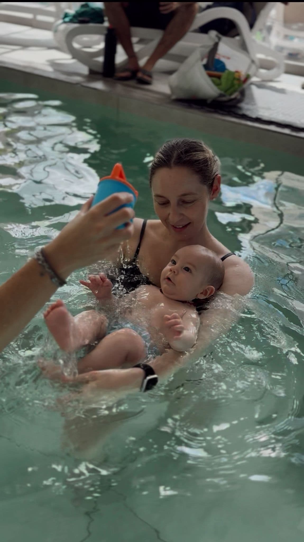 Mamá haciendo flotar a su bebé mientras le cae agua de un vasito